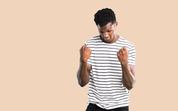 Dark skinned man with striped shirt celebrating a victory and happy for having won a prize on isolated ocher background