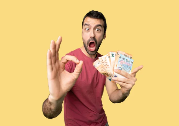 男人拿了很多钱 在孤立的黄色背景上展示确定的标志 并竖起一个大拇指的手势 — 图库照片