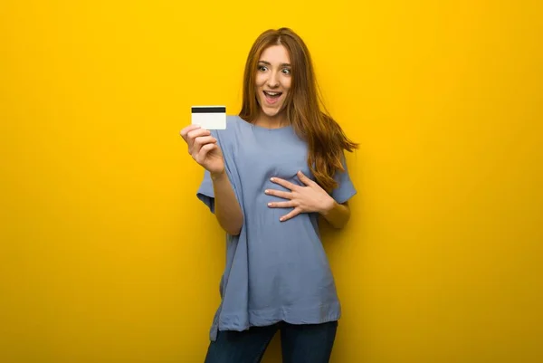 Młoda Ruda Dziewczyna Tle Żółte Ściany Trzymając Kartę Kredytową Zaskoczony — Zdjęcie stockowe