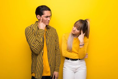 Canlı sarı arka plan üzerinde genç çift kafasına parmak koyarak delilik jest yapma