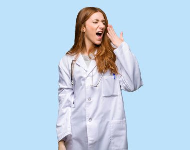 Esneme ve izole mavi zemin üzerine el ile geniş açık ağız kapsayan Kızıl saçlı doktor kadın