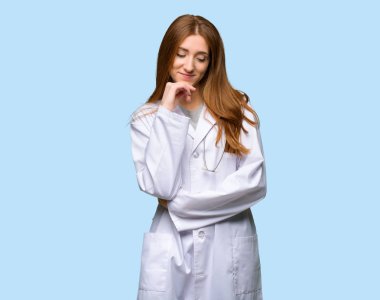 Kızıl saçlı doktor kadın izole mavi arka plan çeneme el ile bakıyor