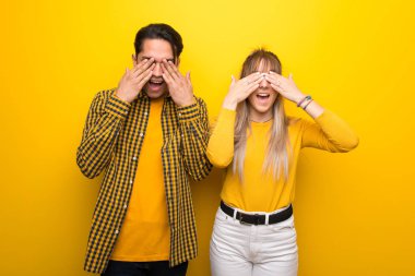 Canlı sarı arka plan üzerinde genç çift elleri ile gözleri kaplayan. İleride ne olduğunu görünce şaşırdım