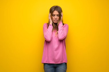 Baş ağrısı ile sarı duvarın üzerinden pembe kazaklı kadın