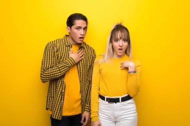 Canlı sarı arka plan üzerinde genç çift şaşırttı ve doğru bakarken şok