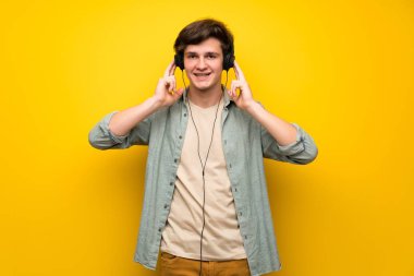 Genç adam sarı duvar kulaklık ile müzik dinlemek