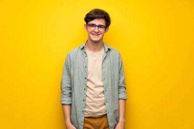 Genç adam gözlüklü ve mutlu sarı duvarın üzerinden