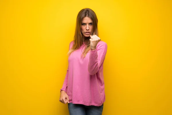 妇女与粉红色毛衣在黄色墙壁以愤怒的姿态 — 图库照片