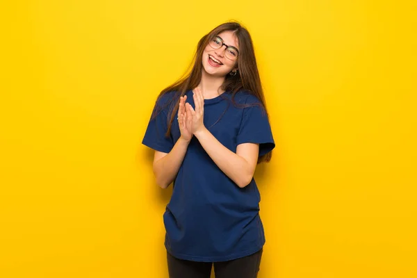 Young woman with glasses over yellow wall applauding after presentation in a conference