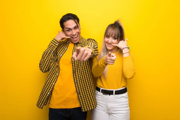 Junges Paar Auf Leuchtend Gelbem Hintergrund Macht Handygeste Und Zeigt — Stockfoto