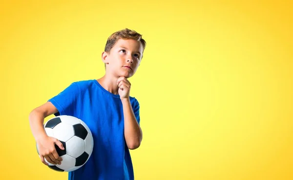 Boy playing soccer and thinking on yellow background