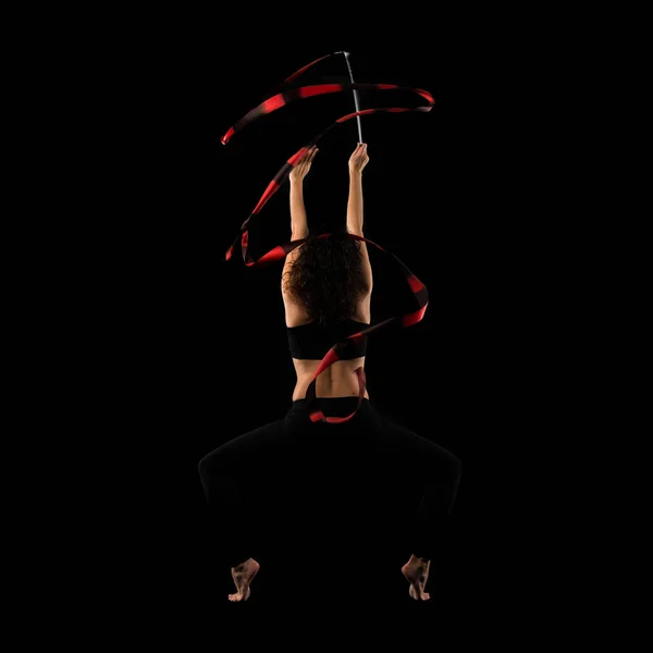 Woman doing rhythmic gymnastics with ribbon on black background