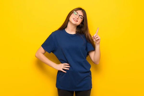 Mujer Joven Con Gafas Sobre Pared Amarilla Mostrando Levantando Dedo — Foto de Stock