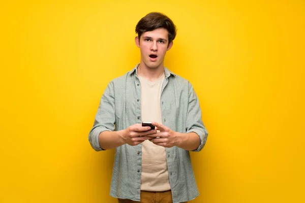 Jugendlicher Mann Über Gelbe Wand Überrascht Und Eine Nachricht Geschickt — Stockfoto