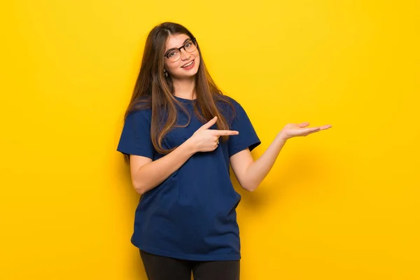 Mladá Žena Brýlemi Nad Žluté Zdi Drží Imaginární Copyspace Dlani — Stock fotografie