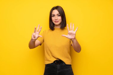 Genç kadın dokuz parmaklı sayma sarı duvarın üzerinden