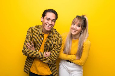 Canlı sarı arka plan üzerinde genç çift gülümseyerek kollarını çapraz tutmak