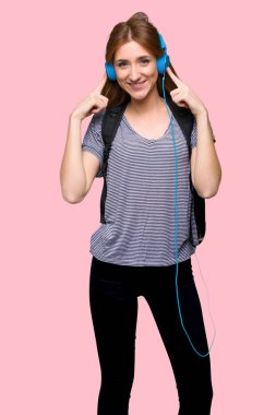 Kızıl saçlı öğrenci kadın izole pembe bir arka plan üzerinde kulaklık ile müzik dinlemek