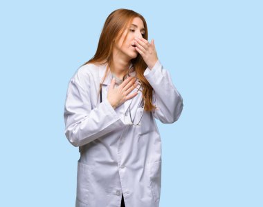 Kızıl saçlı doktor kadın öksürük ile acı ve izole mavi arka plan üzerinde kötü hissediyor