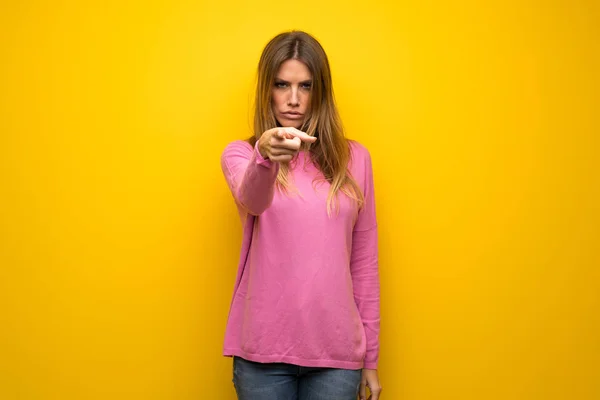 イライラや前方を向く黄色の壁にピンクのセーターの女性 — ストック写真