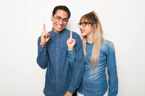 Young couple with glasses showing and lifting a finger in sign of the best