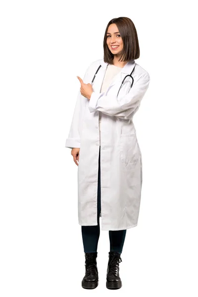 分離の白い背景の上に戻って指している若い医師女性のフルレングス ショット — ストック写真