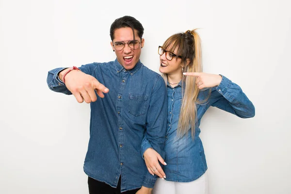 Young couple with glasses frustrated by a bad situation and pointing to the front