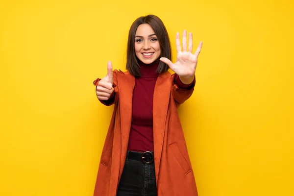 Young woman with coat counting six with fingers