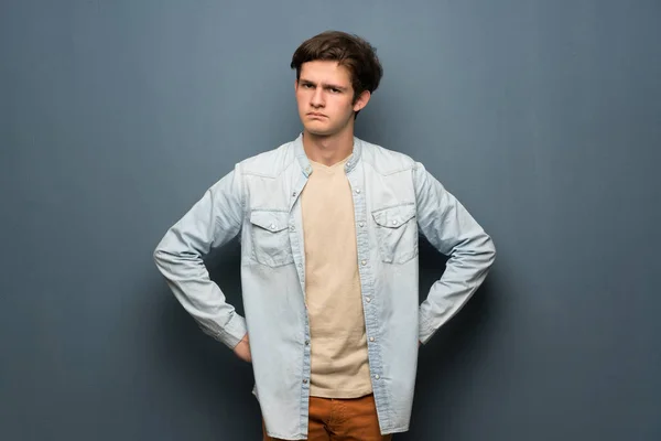 Teenager man with jean jacket over grey wall angry