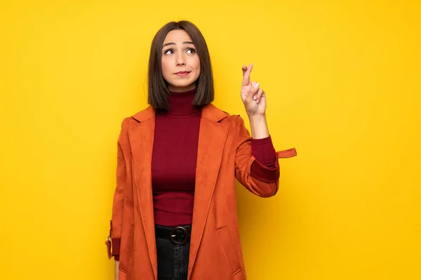 Young woman with coat with fingers crossing and wishing the best