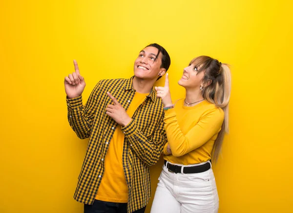 Junges Paar Vor Leuchtend Gelbem Hintergrund Zeigt Mit Dem Zeigefinger — Stockfoto