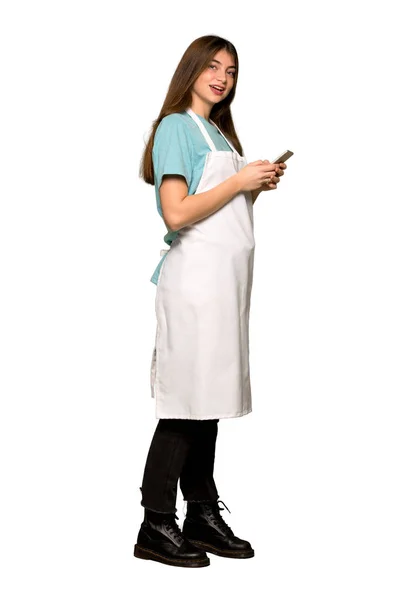 Full-length shot of Girl with apron sending a message with the mobile on isolated white background