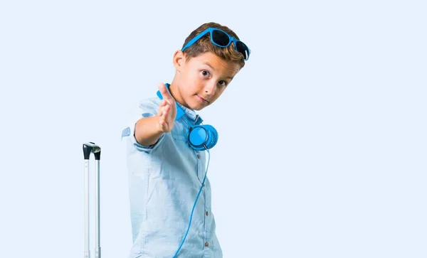 孩子带着太阳镜和耳机在蓝色背景下进行了大量交易后 带着行李箱握手 — 图库照片