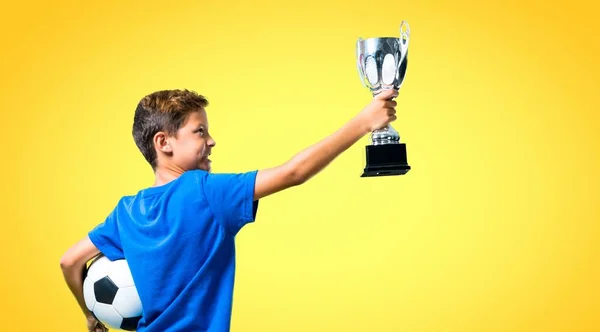 Jongen Voetballen Houden Een Trofee Gele Achtergrond — Stockfoto