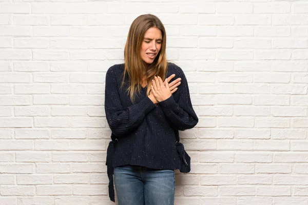 Blonde woman over brick wall having a pain in the heart