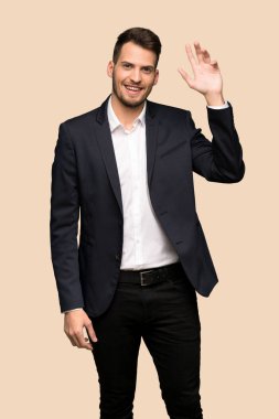 Koyu sarı arka plan üzerinde el ile mutlu ifade ile selamlayan yakışıklı iş adamı