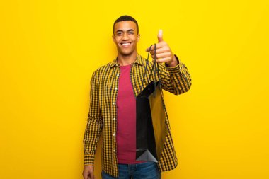 Genç afro Amerikalı adam sarı arka planda çok alışveriş torbaları