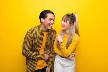 Canlı sarı arka plan üzerinde genç çift göğüs ellerini koyarken çok gülümsüyor