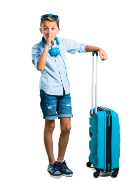 Çocuk tam vücut güneş gözlüğü ve kulaklık bavulunu ağız ve sessizlik bir jest izole beyaz arka plan üzerinde kapanış bir işaret gösteren ile seyahat ile