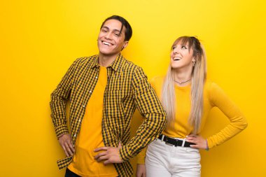 Canlı sarı arka plan üzerinde genç çift kalça kolları ile poz ve gülüyor