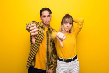 Olumsuz ifade ile başparmak aşağı işareti gösteren canlı sarı arka plan üzerinde genç çift