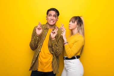 Parmakları geçiş ve en iyi dilek ile canlı sarı arka plan üzerinde Genç çift