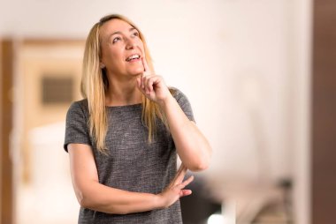 Ayakta ve bir evin içinde ararken bir fikir düşünüyorum gri elbise orta yaş sarışın kadınla