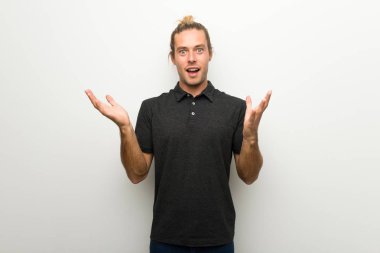 Sürpriz ve şok yüz ifadesi ile beyaz duvarın üzerinden uzun saçlı sarışın adam