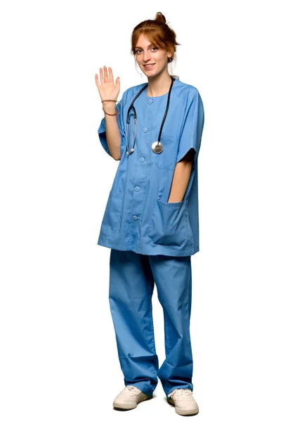 一个年轻的红头发的护士在孤立的白色背景上愉快地用双手敬礼的全长照片 — 图库照片