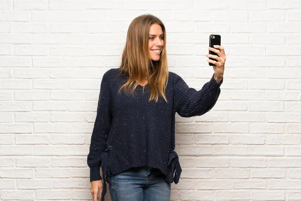 Blonde woman over brick wall making a selfie