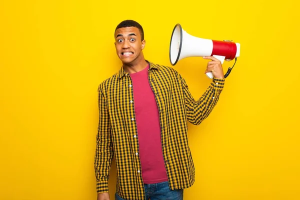 Young afro american man on yellow background taking a megaphone that makes a lot of noise