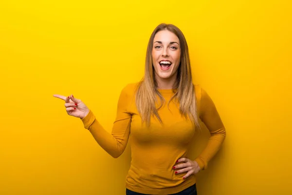 黄色背景側に指を指していると製品を提示の上の若い女性 — ストック写真