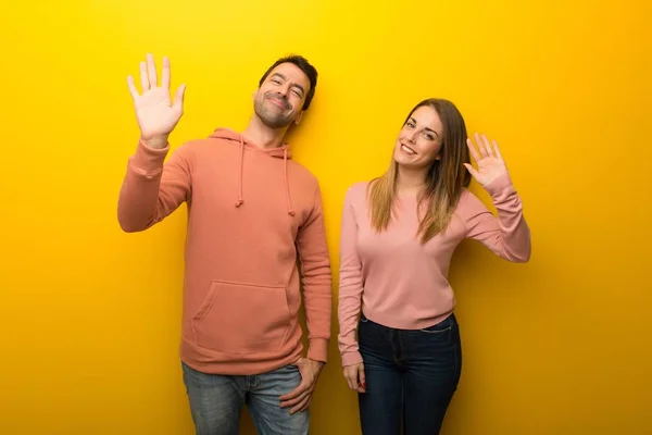 Group of two people on yellow background saluting with hand with happy expression