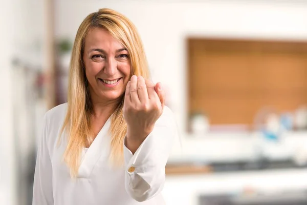 Middle age blonde woman with white shirt presenting and inviting to come with hand. Happy that you came at home